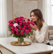 Mujer joven y elegante oliendo un arreglo floral NARCISA de 36 rosas fucsia vibrantes con toques de paniculata y ranúnculo, s