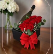 Arreglo floral NATALE con rosas rojas frescas, vino espumoso y lazo rojo en caja negra, ideal para regalo elegante.