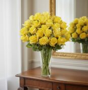 Arreglo floral PANDORA con 36 rosas amarillas frescas en un jarrón de cristal, sobre una mesa de madera elegante con un espej