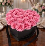 Arreglo Floral Perla con 24 rosas rosadas vibrantes en una caja negra en forma de corazón, sobre una mesa de madera pulida en