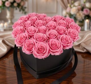Arreglo Floral Perla con 24 rosas rosadas vibrantes en una caja negra en forma de corazón, sobre una mesa de madera pulida en