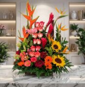 Arreglo floral PIA exótico con rosas, girasoles, aves del paraíso y lirios en tonos vibrantes sobre mármol.