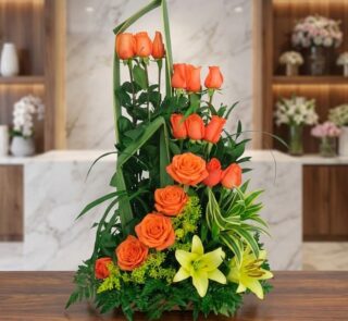 Arreglo Floral Romeo con rosas naranjas abiertas, lirios amarillos y follaje verde exuberante, sobre una superficie de mármol