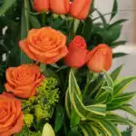 Primer plano extremo de un Arreglo Floral Romeo con rosas naranjas vibrantes, gotas de rocío sutiles y follaje verde, destaca