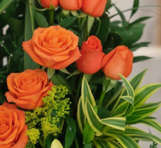 Primer plano extremo de un Arreglo Floral Romeo con rosas naranjas vibrantes, gotas de rocío sutiles y follaje verde, destaca