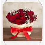 Arreglo floral 'Lidia' con 15 rosas rojas premium en un balde rústico de madera, adornado con un lazo rojo y follaje blanco,