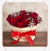 Arreglo floral 'Lidia' con 15 rosas rojas premium en un balde rústico de madera, adornado con un lazo rojo y follaje blanco,