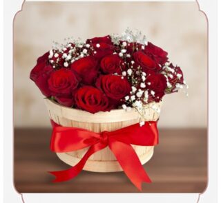 Arreglo floral 'Lidia' con 15 rosas rojas premium en un balde rústico de madera, adornado con un lazo rojo y follaje blanco,