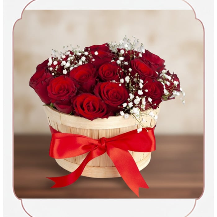 Arreglo floral 'Lidia' con 15 rosas rojas premium en un balde rústico de madera, adornado con un lazo rojo y follaje blanco,
