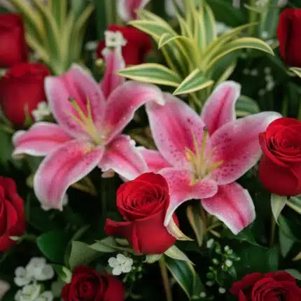 Primer plano extremo de un arreglo floral 'Siempre Juntos' con lirios rosados y rosas rojas, mostrando texturas hiperrealista