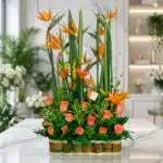 Arreglo floral exótico Suspiro con aves del paraíso, lirios naranjas y rosas melocotón, sobre mármol en floristería premium.