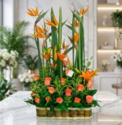 Arreglo floral exótico Suspiro con aves del paraíso, lirios naranjas y rosas melocotón, sobre mármol en floristería premium.
