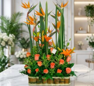 Arreglo floral exótico Suspiro con aves del paraíso, lirios naranjas y rosas melocotón, sobre mármol en floristería premium.