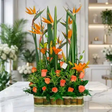 Arreglo floral exótico Suspiro con aves del paraíso, lirios naranjas y rosas melocotón, sobre mármol en floristería premium.