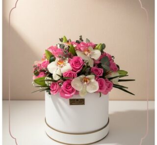 Arreglo floral TANIA con rosas rosadas vibrantes y orquídeas blancas delicadas en una caja redonda blanca con borde dorado, i