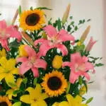 Primer plano extremo de un arreglo floral tropical con lirios rosas, girasoles vibrantes y lirios amarillos, destacando textu