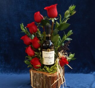 Arreglo floral VERITA con rosas rojas frescas y una botella de vino tinto, presentado en una base de madera rústica, ideal pa