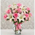 Arreglo floral vibrante con rosas rosadas, lirios blancos y claveles rosados en un jarrón de cristal con lazo rosa, ideal par