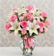 Arreglo floral vibrante con rosas rosadas, lirios blancos y claveles rosados en un jarrón de cristal con lazo rosa, ideal par