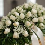 Fotografía macro premium del Arreglo Fúnebre Cubre Caja Cielo, con rosas blancas, follaje verde y rocío sutil. Detalle de cin