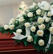 Fotografía macro premium del Arreglo Fúnebre Cubre Caja Misericordia, con rosas blancas, follaje verde y rocío sutil, sobre u