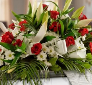 Arreglo fúnebre cubre caja Paraíso con rosas rojas, lirios blancos y margaritas, con follaje verde y cinta satinada.