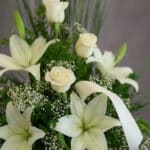 Fotografía macro premium del Arreglo Fúnebre Descanso Eterno, mostrando lirios y rosas blancas con rocío sutil, follaje verde