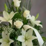 Fotografía macro premium del Arreglo Fúnebre Descanso Eterno, mostrando lirios y rosas blancas con rocío sutil, follaje verde