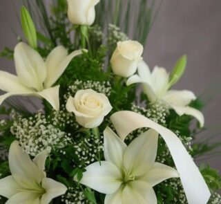 Fotografía macro premium del Arreglo Fúnebre Descanso Eterno, mostrando lirios y rosas blancas con rocío sutil, follaje verde