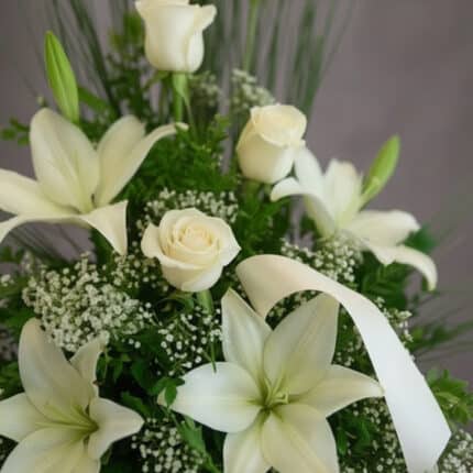 Fotografía macro premium del Arreglo Fúnebre Descanso Eterno, mostrando lirios y rosas blancas con rocío sutil, follaje verde
