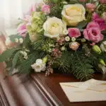 Primer plano de un arreglo floral fúnebre con rosas blancas, rosas y lirios, follaje verde, rocío sutil, cinta satinada y sob