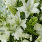 Primer plano extremo de un arreglo fúnebre inmortal con lirios blancos, rosas y follaje verde, mostrando gotas de rocío y tex