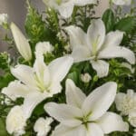 Fotografía macro premium del Arreglo Fúnebre Piedad, mostrando lirios blancos y claveles con rocío sutil, follaje verde y una