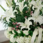 Fotografía macro premium del Arreglo Fúnebre Te Fuiste, mostrando lirios y rosas blancas con rocío sutil, follaje verde y peq