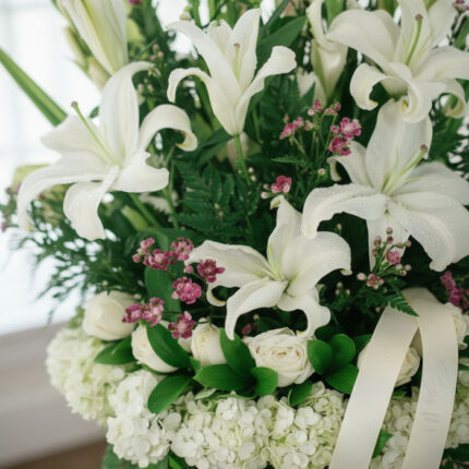 Fotografía macro premium del Arreglo Fúnebre Te Fuiste, mostrando lirios y rosas blancas con rocío sutil, follaje verde y peq