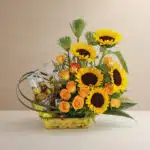 Arreglo floral vibrante con girasoles, rosas naranjas y cuatro botellas de cerveza Corona en una base amarilla, ideal para ce