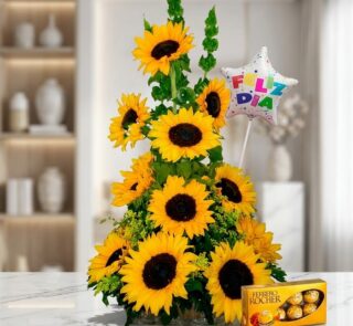 Arreglo floral exótico con girasoles grandes y vibrantes, follaje verde, un globo de 'Feliz Día' y una caja de chocolates Fer