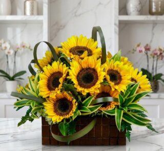 Arreglo floral exótico con girasoles Soleil grandes y abiertos, hojas verdes vibrantes, en una cesta de madera oscura sobre m