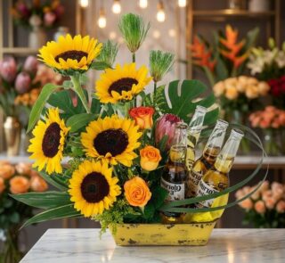 Arreglo floral exótico y vibrante con girasoles grandes y abiertos, rosas naranjas, proteas y hojas de monstera, acompañado d