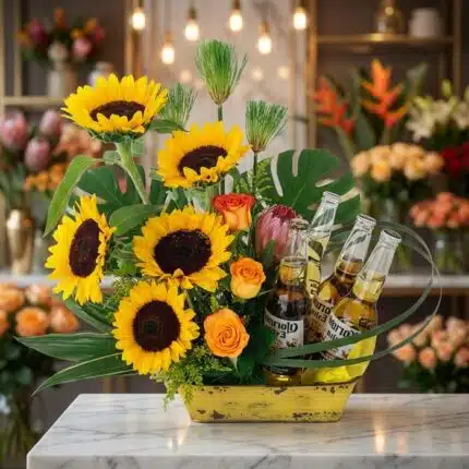 Arreglo floral exótico y vibrante con girasoles grandes y abiertos, rosas naranjas, proteas y hojas de monstera, acompañado d