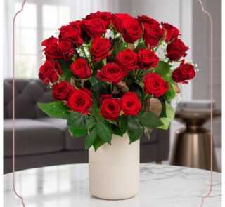 Arreglo floral Jianna con 25 rosas rojas frescas en un elegante jarrón blanco sobre mesa de mármol, fondo difuminado de sala