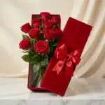 Caja premium de terciopelo rojo con 12 rosas rojas de exportación, frescas y con gotas de rocío, sobre una mesa de mármol bla