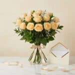 Bouquet de 12 rosas Celestina color melocotón, atado con cinta de satén, junto a una tarjeta de regalo elegante en un sobre a