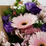 Primer plano extremo de un bouquet floral CARINA con gerberas rosadas, astromelias y lisianthus morados, destacando texturas