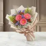 Bouquet Floral LIA con gerberas amarillas vibrantes, envuelto en papel coreano elegante, sobre una superficie de mármol pulid