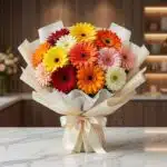 Bouquet de gerberas multicolor vibrantes, envuelto en papel crema elegante con lazo de satén, sobre una mesa de mármol en un