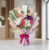 Bouquet de Flores GIA con gerberas rosadas, lirios blancos y flores moradas, envuelto en papel coreano elegante y lazo fucsia