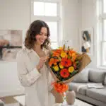 Mujer joven sonriente admirando un Bouquet Floral LIRICA con lirios naranjas y rosas amarillas, envuelto en papel kraft con m