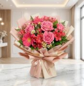 Bouquet ORLENA con rosas rosadas, gerberas fucsia y alstroemerias rojas, envuelto en papel coreano rosa claro sobre mármol bl