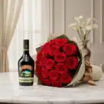 Elegante bouquet de rosas rojas frescas y una botella de Baileys original, presentado sobre una superficie de mármol en un en